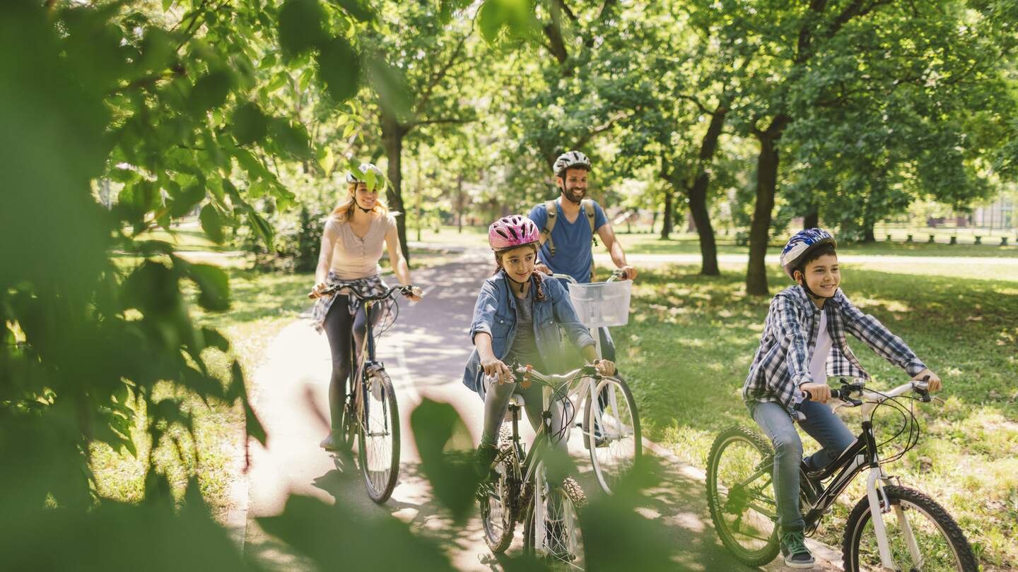 Mutter, Vater, und zwei Kinder fahren im Wald Fahrrad und tragen alle Fahrradhelme. | © Gettyimages.com/vgajic Miodrag Gajic