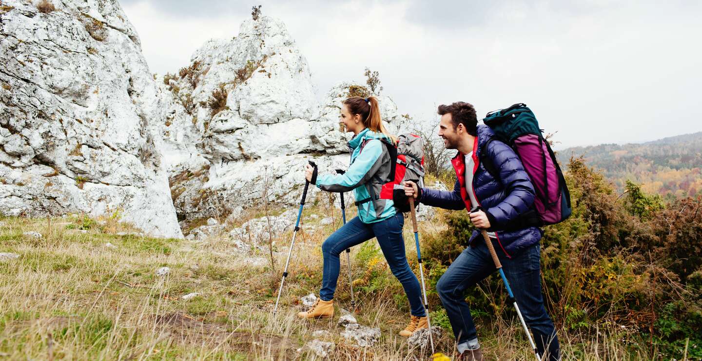 glückliches Paar mit Rucksack beim Bergwandern mit Felsen im Hintergrund | © Gettyimages.com/BartekSzewczyk