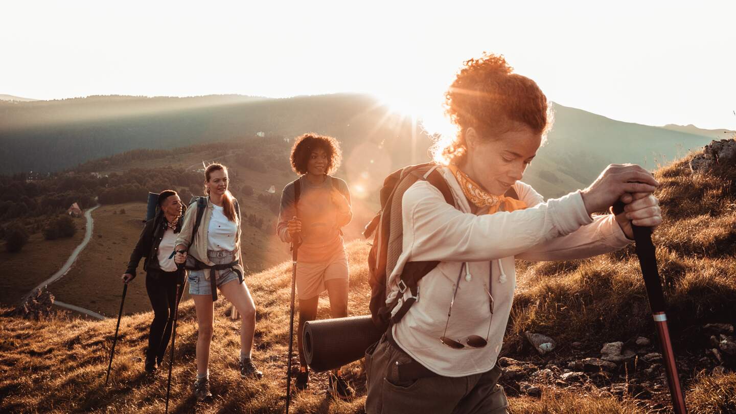 Vier Wanderer sind auf einem Bergpfad unterwegs, waehrend die Sonne tief am Horizont steht  | © gettyimages.com/Geber86