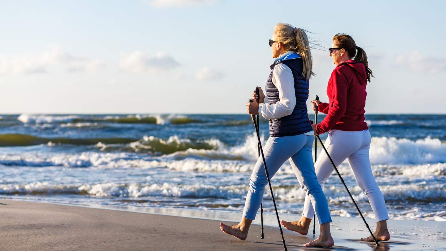 Zwei Frauen machen Nordic Walking am Strand an der Ostsee mit Brandung im Hintergrund bei Sonnenschein | © © Gettyimages.com/gbh007