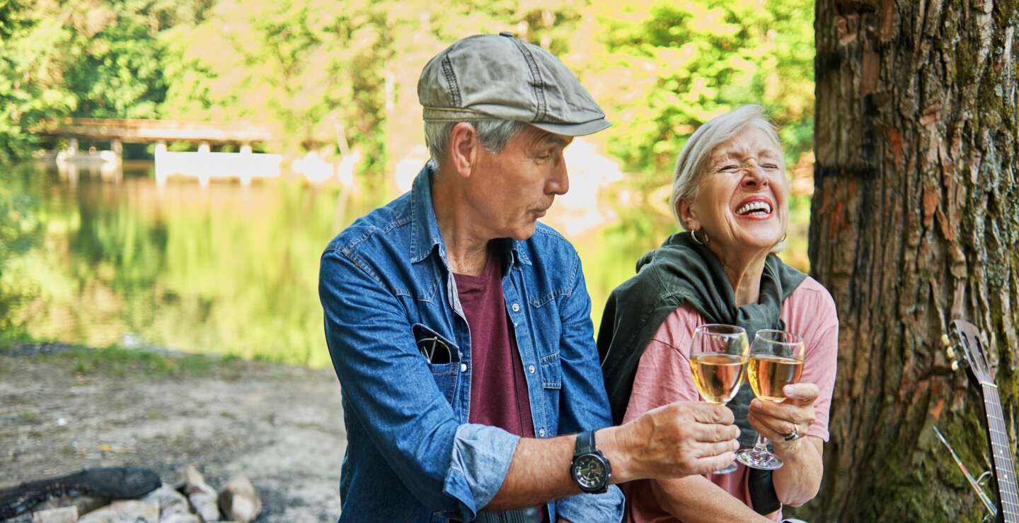 Paar sitzt auf einem Baumstamm und stößt mit Weißwein an | ©  © Gettyimages.com/DaniloAndjus