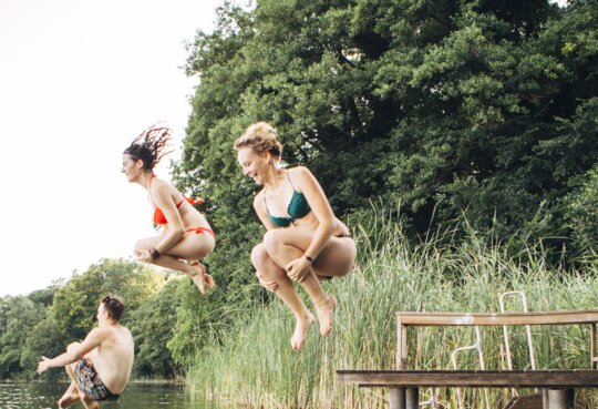 Drei junge Menschen springen in See  | © Gettyimages.com/fotografixx
