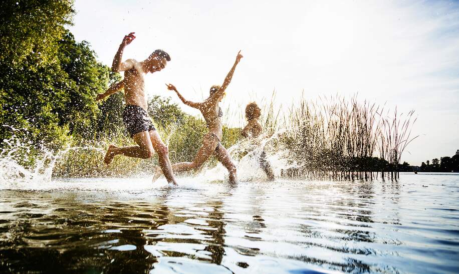 Eine Gruppe von Freunden, die an einem gemeinsamen Tag am See aufgeregt im Wasser planscht. | © Gettyimages.com/TommL