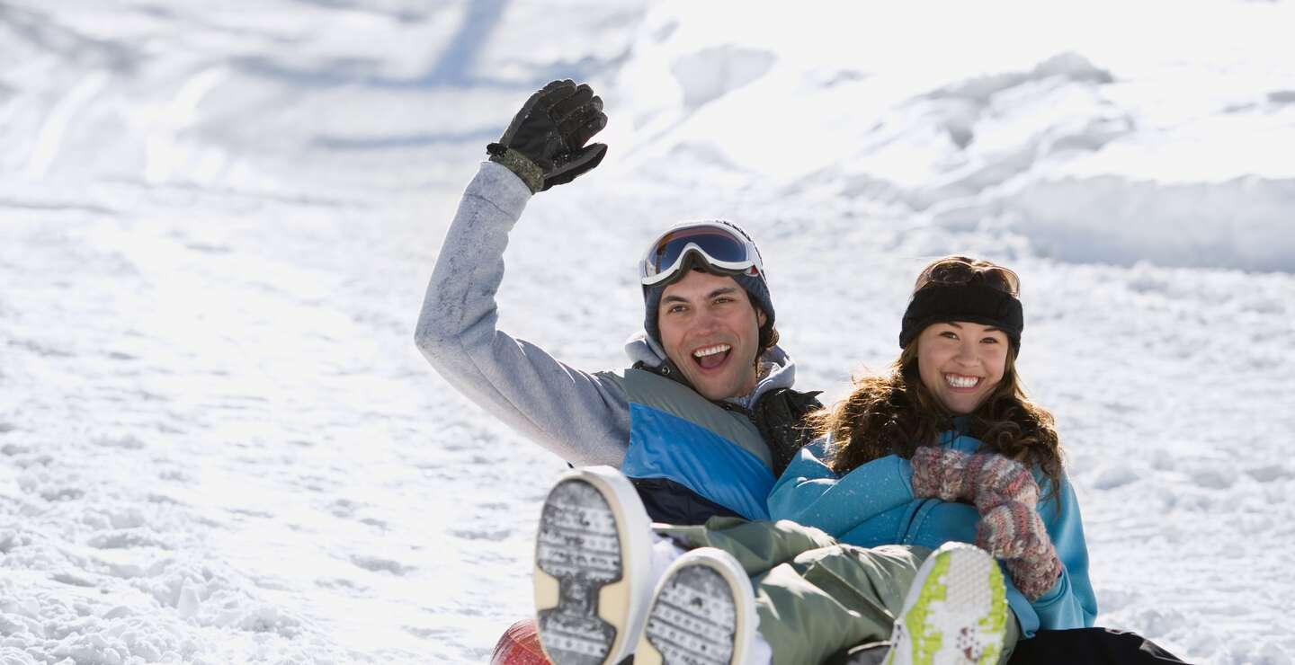 Zwei Personen rodeln einen verschneiten Huegel hinunter. | © gettyimages.com/image source