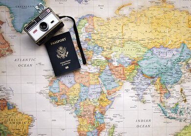 Auf einer bunten Weltkarte liegen ein altmodischer Fotapparat und ein Reisepass | © Pixabay/Pamjpat