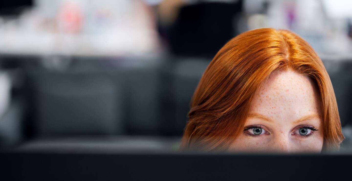 Das Gesicht einer rothaarigen Frau ragt über einen Bildschirm in einem Büro | © Pixabay.com/raeng_publications