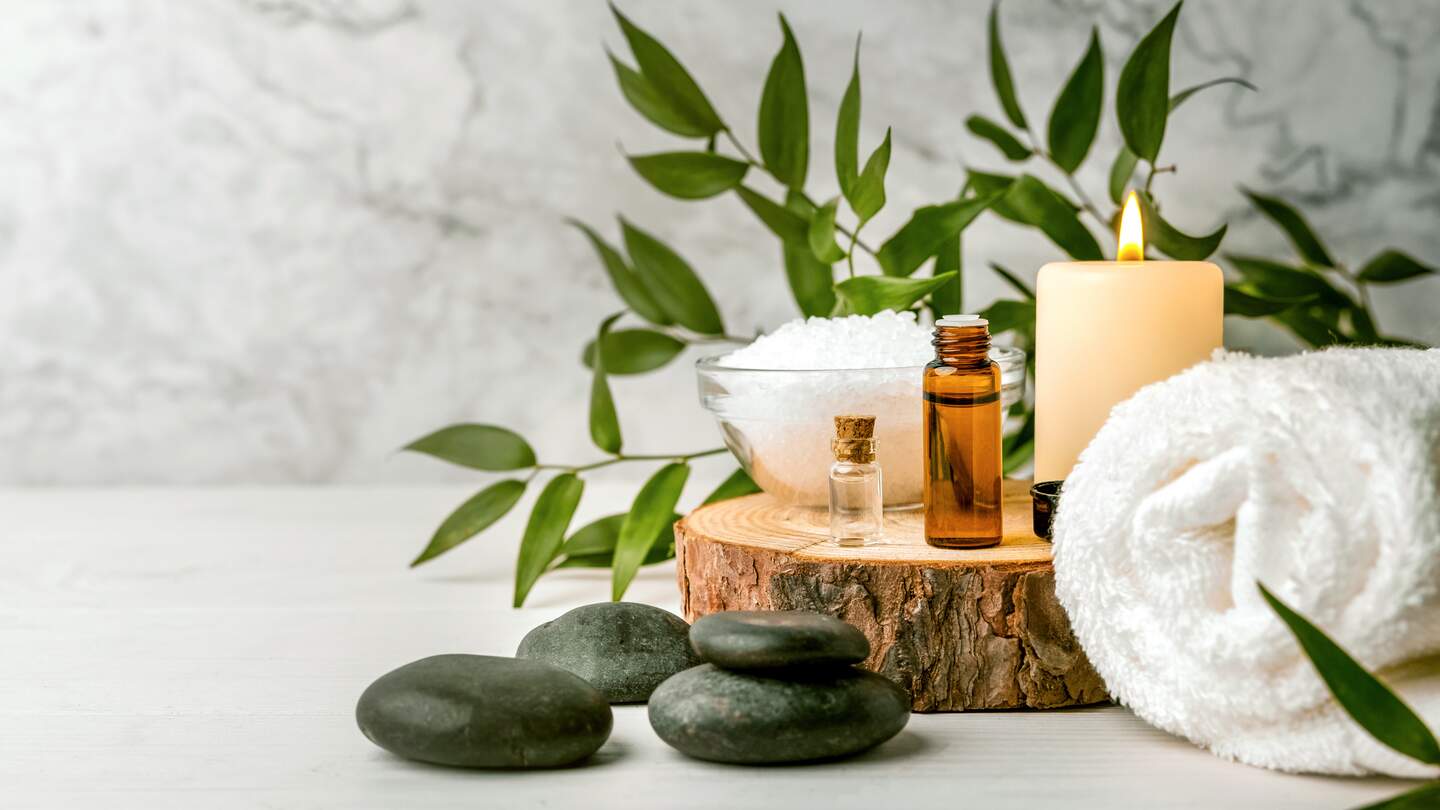 Schönheitsbehandlungen für Spa-Verfahren auf weißem Holztisch. Massagesteine, ätherische Öle und Meersalz | © Gettyimages.com/ronstik