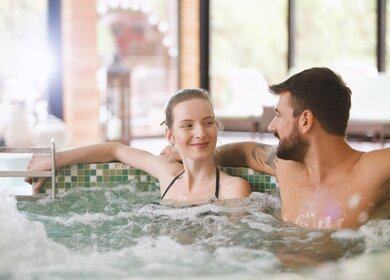 Glueckliches Paar sitzt in einem Whirlpool im Spa-Resort | © Gettyimages.com/fotostorm