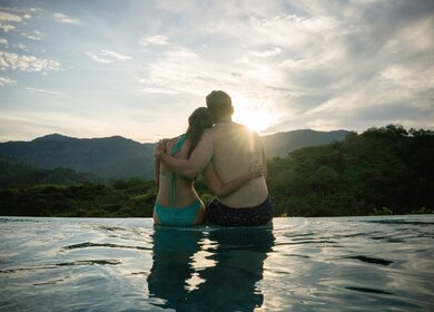 Paar betrachtet den Sonnenuntergang im Infinity Pool – romantische Kurzurlaubskonzepte | © Gettyimages.com/andresr