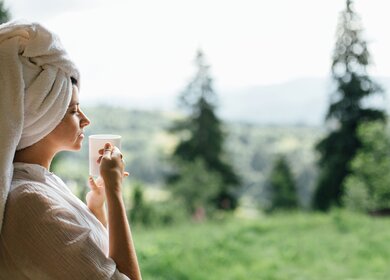 Schöne junge Frau, die am sonnigen Morgen Kaffee vor dem Hintergrund der Berghügel genießt. | © GettyImages.com/Bogdan Kurylo