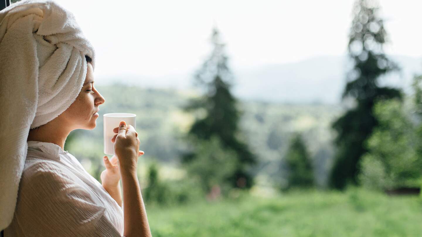 Schöne junge Frau, die am sonnigen Morgen Kaffee vor dem Hintergrund der Berghügel genießt. | © GettyImages.com/Bogdan Kurylo