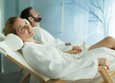 Frau und Mann in weißen Bademänteln entspannen auf Wellnessliegen | © Gettyimages.com/nd3000;