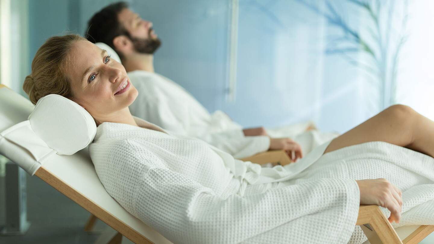 Frau und Mann in weißen Bademänteln entspannen auf Wellnessliegen | © Gettyimages.com/nd3000;