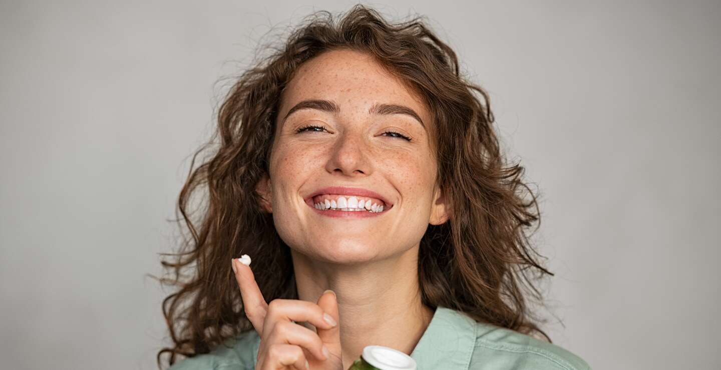Schöne lächelnde Frau Anwendung Gesichtscreme aus grünem Glas | © © Gettyimages.com/Ridofranz