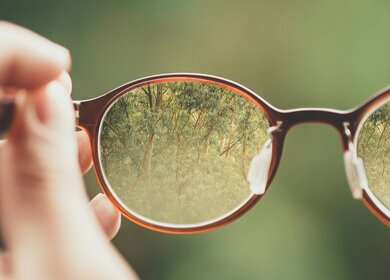  Person mit brauner Brille mit grünem Baumhintergrund | © Unsplash/Bud Helisson 