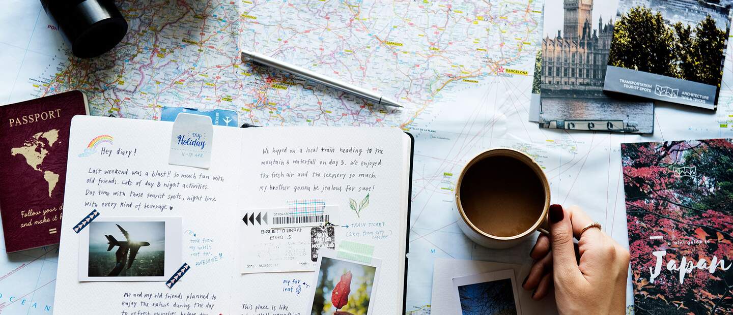 eine flache Anordnung verschiedener Reiseutensilien auf einer Oberflaeche, darunter eine Karte, ein Fernglas, ein Reisepass, Postkarten, Fotos und eine Tasse Kaffee | © gettyimages.com/Rawpixel Ltd.