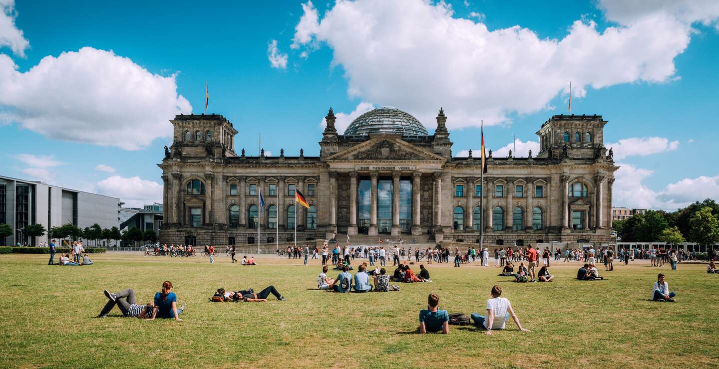 Blick auf das deutsche Parlament in Berlin, genannt Reichstag. Die Menschen ruhen sich aus und liegen auf der Wiese. | © Gettyimages.com/Nikada