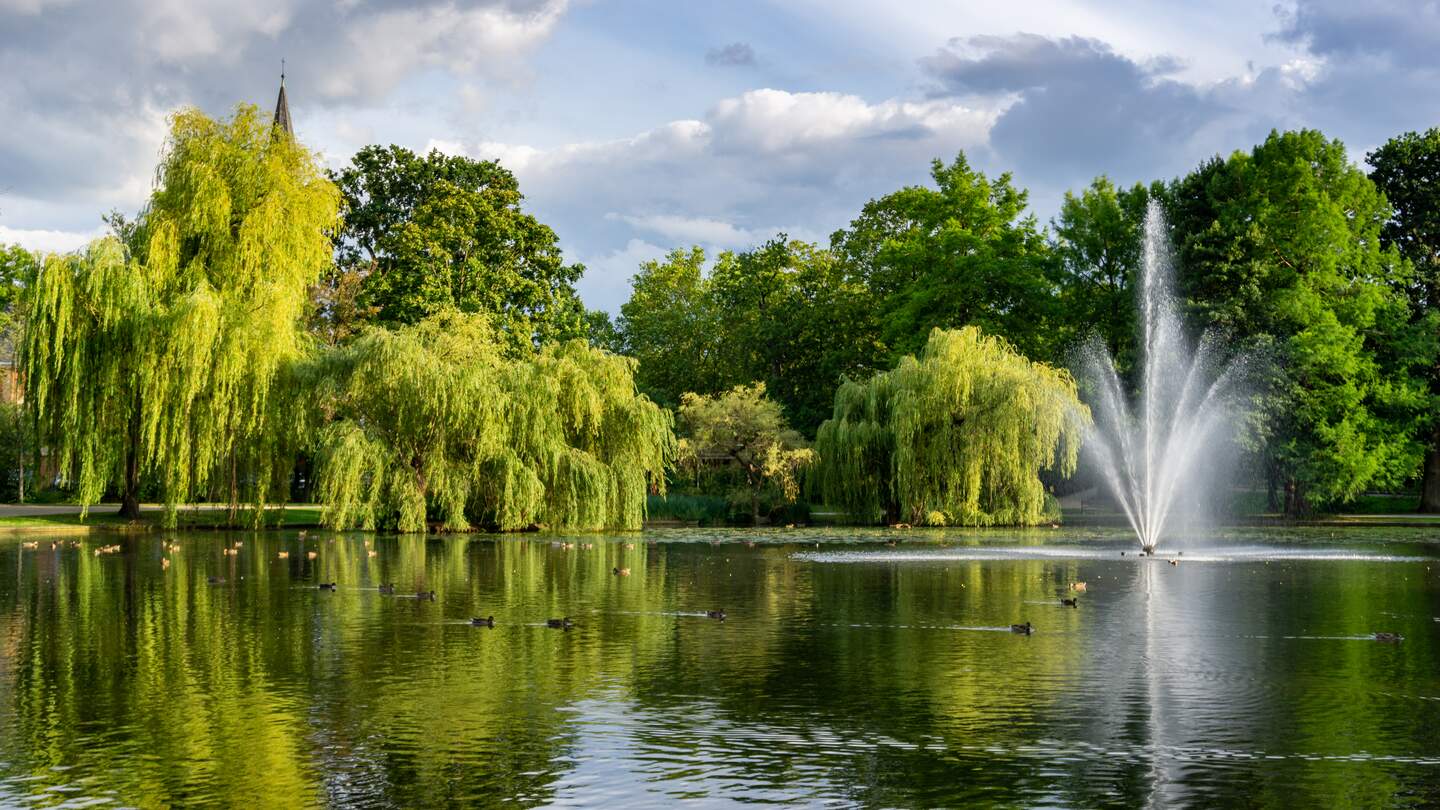 Blick auf wunderschöne Stadtgärten und Park mit Teich und Geysirbrunnen bei gutem Wetter | © GettyImages.com/troyka