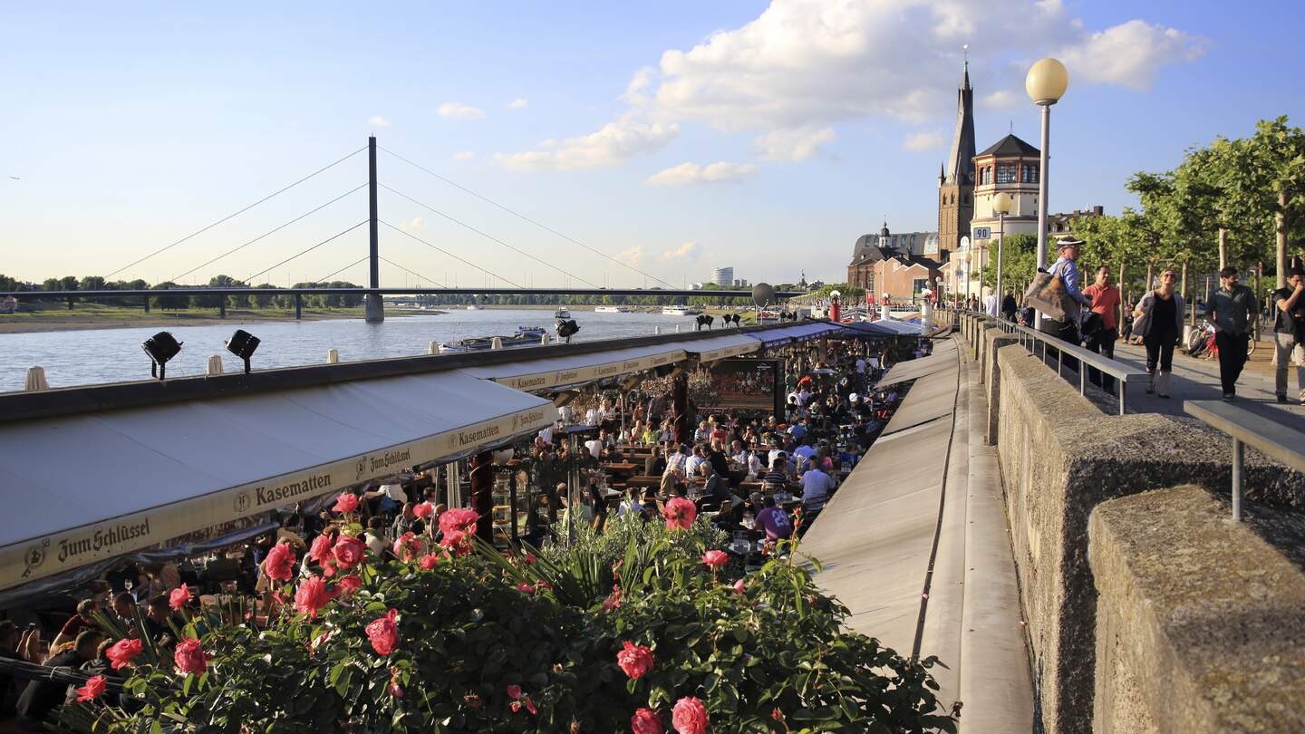Bars und Restaurants entlang des Rheins in Düsseldorf und Menschen, die auf der Promenade darüber spazieren gehen | © Gettyimages.com/Lux_D