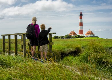 Leuchtturm Westhever, Schleswig-Holstein | © Gettyimages.com/no_limit_pictures Frau und Junge stehen auf einer kleinen Bruecke und schauen in Richtung des Leuchturms von Westhever | © Gettyimages.com/no_limit_pictures