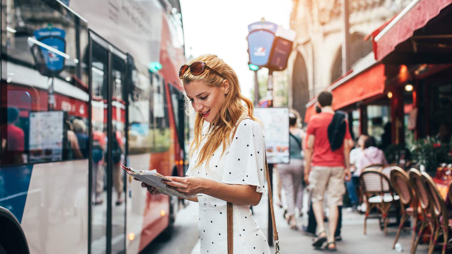 Schöne, junge Frau in Paris macht eine Bustour, eine Stadtkarte in der Hand haltend  | © Gettyimages.com/Jasmina007