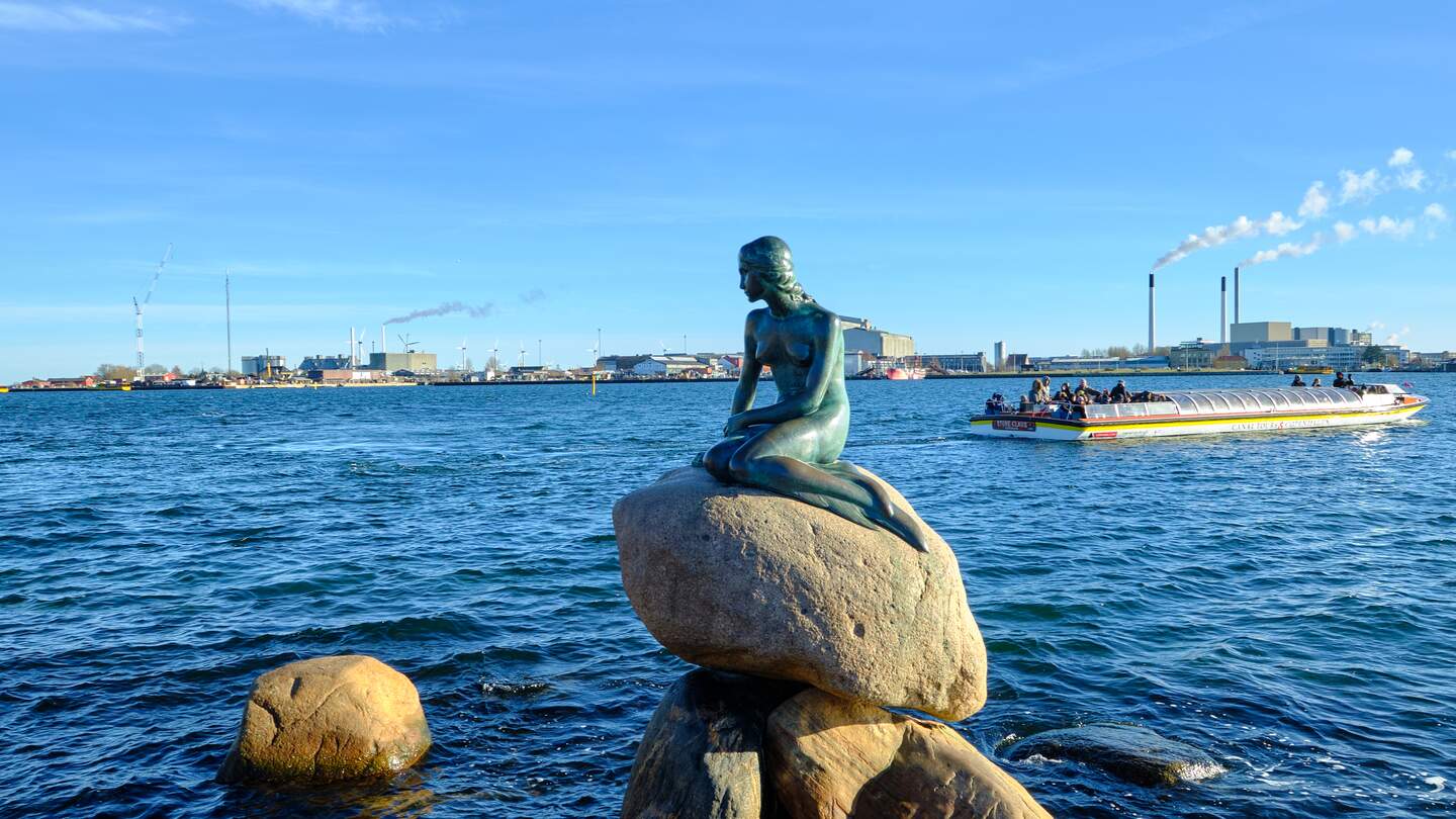Statue der kleinen Meerjungfrau in Kopenhagen mit Touristenboot und Verbrennungsanlage im Hintergrund | © Gettyimages.com/Angelafoto