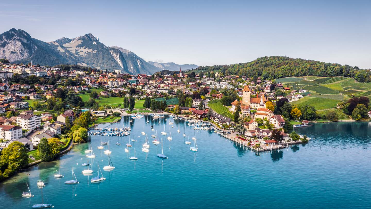 Blick auf den Thuner See, im Hintergrund ist ein Dorf und dahinter Berge. Das Schloss Spiez ist zu sehen. | © Gettyimages.com/JaCZhou