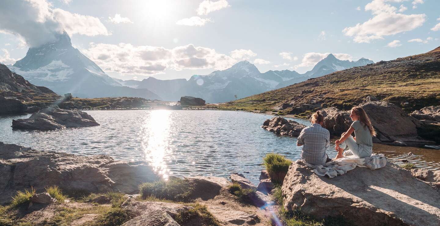 Paar geniesst am Seeufer den Sonnenuntergang mit Blick auf das Matterhorn in den Schweizer Alpen | © Gettyimages.com/Mystockimages Paar geniesst am Seeufer den Sonnenuntergang mit Blick auf das Matterhorn in den Schweizer Alpen | © Gettyimages.com/Mystockimages