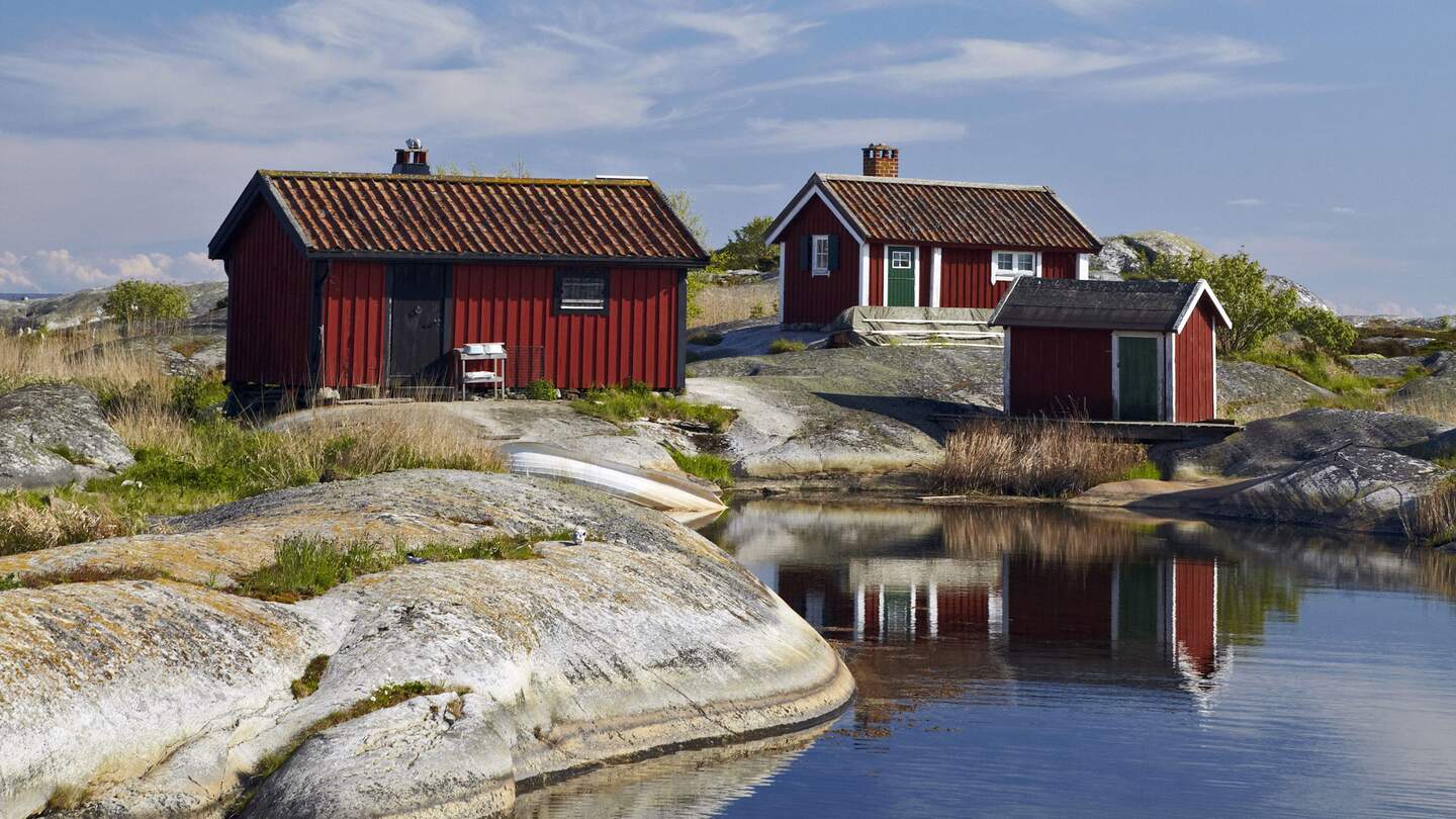 Drei rote Holzhütten mit weißen Fensterrahmen stehen auf Felsen am Wasser. | © imagebank.sweden.se/Ola Ericson