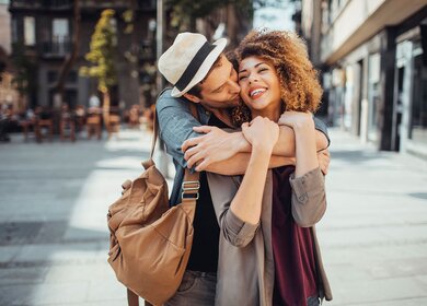 Ein glückliches, junges Paar umarmt sich auf einem Platz vor einem Staßencafe | © © Gettyimages.com/Geber86