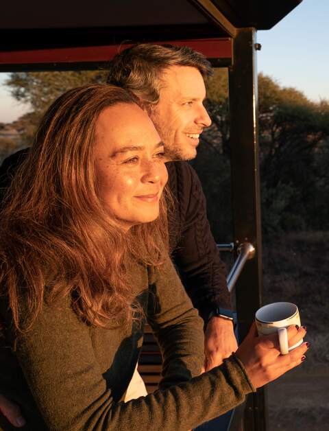 Ein Paar steht während des Sonnenunterganges auf dem Balkon des Rovos Rails in Afrika  | © © Greg Beadle 