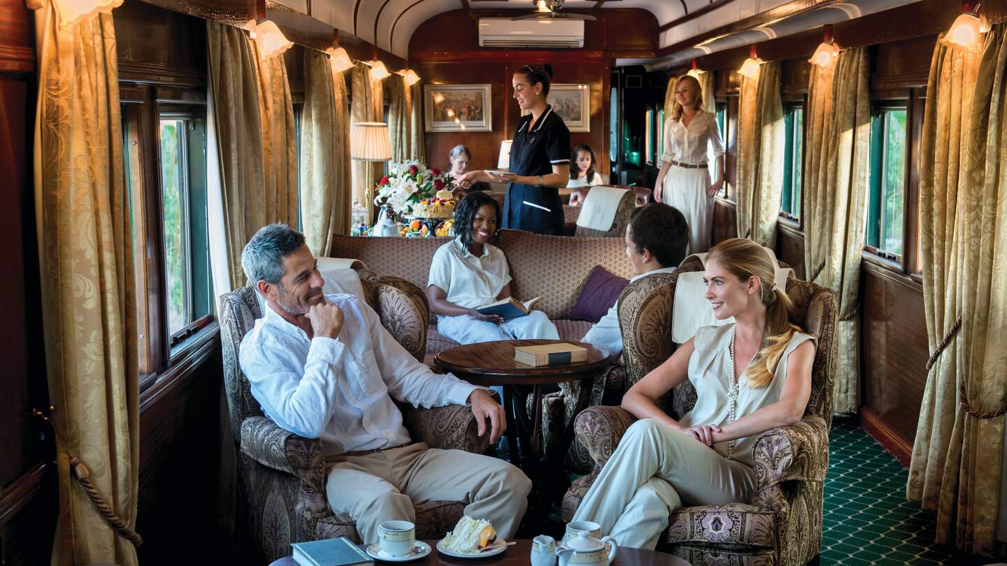 Passagiere sitzen im Rovos Rail in Afrika in einem Lounge-Waggon und werden von einer Mitarbeiterin bedient. | © © DOOKPHOTO