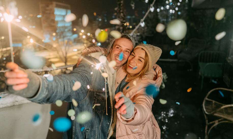 Junges Paar mit Wunderkerzen, die die schneereiche Silvesternacht zusammen genießen. | © © Gettyimages.com/AleksandarNakic