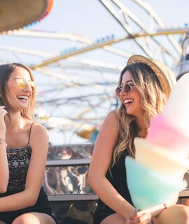 Spass im Freizeitpark: Freundinnen geniessen Zuckerwatte vor Achterbahnkulisse | © gettyimages.com/DusanManic