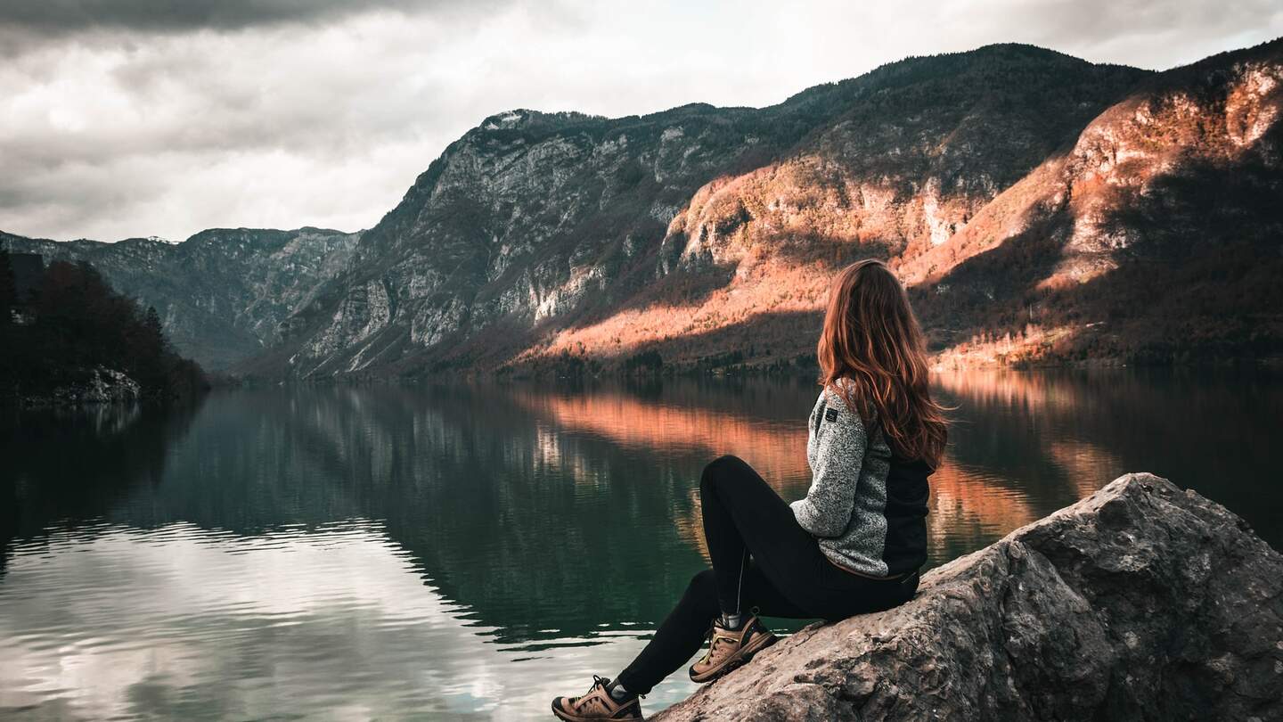Ruhige Reflexion am See | © Pixabay.com/sallycadore Eine Frau die auf einem grossen Felsen am Rand sitzt und auf eine Bergenlandschaft blickt | © Pixabay.com/sallycadore