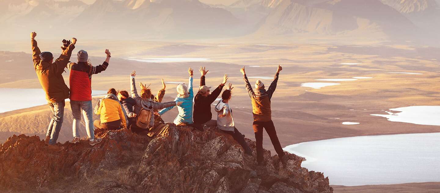 Eine große Gruppe glücklicher Freunde in gemischtem Alter bejubelt den gemeinsamen Aufstieg zum Berggipfel | © Gettyimages.com/molchanovdmitry