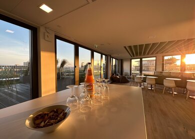 Lounge bei Ameropamit mit Saft, Gläsern und Kesen im Vordergrund sowie meheren Tischen und Stühlen sowie Zugang zur Dachterrasse im Hintergrund | © Ameropa/Verena Cezanne