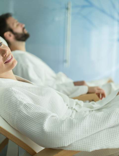 Frau und Mann in weißen Bademänteln entspannen auf Wellnessliegen | © Gettyimages.com/nd3000;
